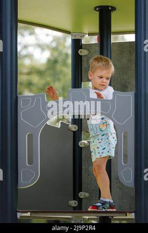 Der kleine Junge klettert hoch zum Aussichtsturm auf dem Spielplatz. Stockfoto