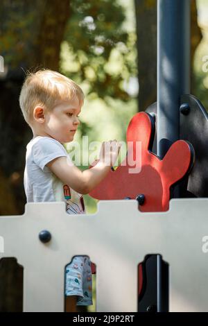 Ein süßer, urkomischer, blonder Junge spielt auf einem Spielplatz im Freien und fährt ein Piratenschiff. Stockfoto