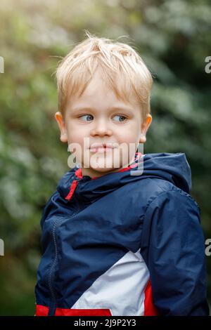 Ein Porträt eines fröhlichen kleinen, niedlichen Jungen aus der Nähe der Natur vor grünem Hintergrund. Vertikales Foto. Stockfoto