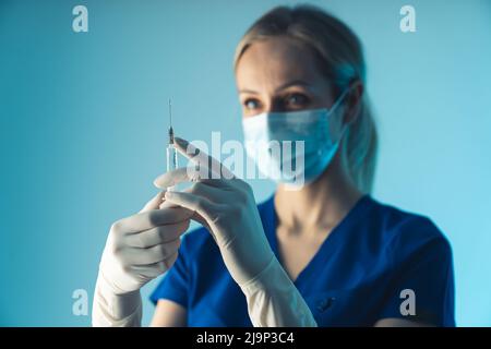Nahaufnahme des Studios auf blauem Hintergrund einer fokussierten blonden kaukasischen Ärztin mit einer Spritze. Impfkonzept. Hochwertige Fotos Stockfoto