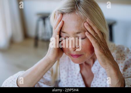 Porträt einer attraktiven älteren Frau, die zu Hause mit Kopfschmerzen auf einem Sofa sitzt Stockfoto