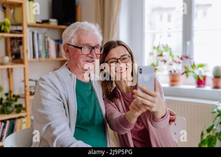 Erwachsene Tochter besucht ihren älteren Vater zu Hause und nimmt Selfie. Stockfoto