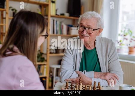 Erwachsene Tochter besucht ihren älteren Vater zu Hause und spielt gemeinsam Schach. Stockfoto
