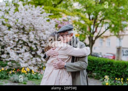 Erwachsene Tochter umarmte ihren älteren Vater im Park am Frühlingstag. Stockfoto