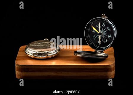 Antike Kompass- und Taschenuhr auf Holz mit schwarzem Hintergrund. studiolicht Stockfoto