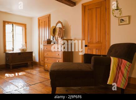 Brauner gepolsterter langer Stuhl und antike Kommode mit Spiegel im oberen Schlafzimmer im alten, ca. 1741 Jahre alten Haus im kanadischen Cottage-Stil. Stockfoto