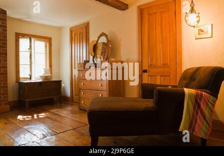 Brauner gepolsterter langer Stuhl und antike Kommode mit Spiegel im oberen Schlafzimmer im alten, ca. 1741 Jahre alten Haus im kanadischen Cottage-Stil. Stockfoto