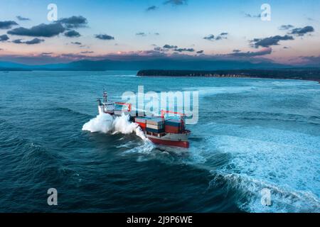 Stürmische See mit Containerschiff, das bei Sonnenuntergang Fracht liefert Stockfoto
