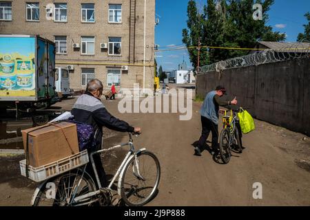 23. Mai 2022, Severodonetsk, Ukraine: Zivilisten sehen, wie sie das Zentrum der Verteilung der humanitären Hilfe der Stadt mit Kisten humanitärer Hilfe verlassen. Severodonetsk, die größte Stadt unter ukrainischer Kontrolle in der Provinz Luhansk, ist von der russischen Armee unter heftigen Artillerie- und Raketenbeschuss geraten. Die Stadt ist fast vom Rest der Region isoliert, es gibt eine Hauptstraße, die die Stadt mit Kramatorsk verbindet, die russische Armee versucht, sie zu besetzen und zu kontrollieren, um die Versorgung der Stadt zu reduzieren. Militärexperten schlagen die Möglichkeit vor, dass Severodonetsk unter Belagerung fallen könnte, so die Stockfoto