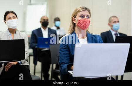 Junge Geschäftsfrau in Maske, die während einer Geschäftskonferenz am Laptop arbeitet Stockfoto