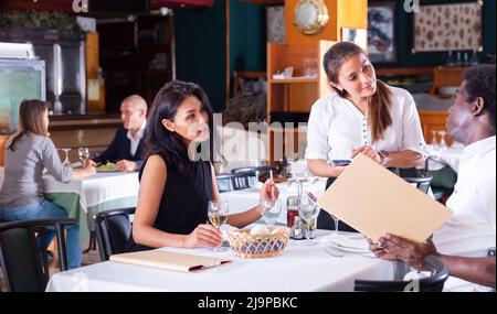 Positive weibliche Busboy nimmt Auftrag zu paar in modernen Restaurante Stockfoto