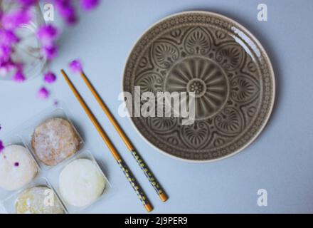 Traditionelles japanisches Dessert-Mochi in Reisteig oder Daifuku. Mochi-Eiskugeln und grauer runder Teller, Essstäbchen auf blauem Hintergrund flach. Ta Stockfoto