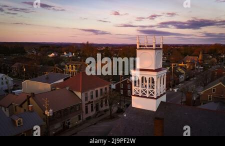 Luftaufnahme eines Sonnenaufgangs in einer Kleinstadt mit Licht, das über Horizon kommt, an einem wunderschönen Frühlingsmorgen in der Nähe eines Kirchturm Stockfoto