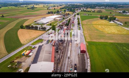Drohne Blick auf eine Dampfgaststation und einen Frachthof mit Rollmaterial und leeren Gleisen an einem wolkigen Sommertag