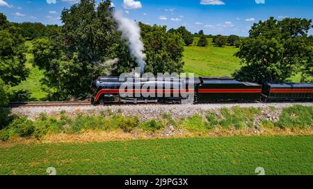 Seitliche Luftaufnahme einer Dampflokomotive, die an einem schönen Sommertag Rauch aufbläst Stockfoto