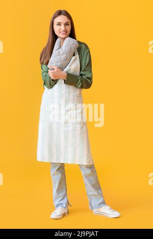 Hübsche junge Frau mit Ofenhandschuh auf gelbem Hintergrund Stockfoto