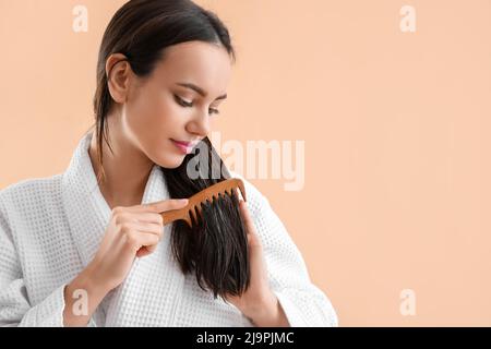 Junge Frau putzt ihre Haare mit Kokosöl auf beigem Hintergrund Stockfoto