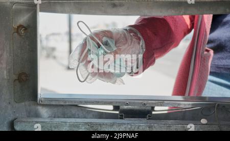 Frau mit Handschuhen wirft eine schützende medizinische Maske gegen Viren in den Müll Stockfoto