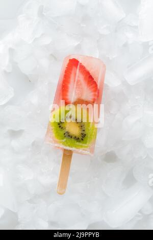 Eine einzelne Erdbeer-Kiwi-Popsicles, isoliert auf einem Eisbett. Stockfoto