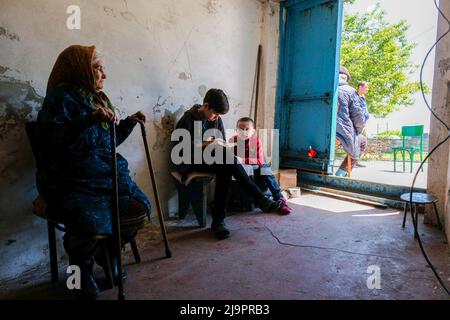 Eine alte Frau sitzt neben zwei Kindern am Eingang des Bunkers, wo sie in den Außenbezirken der Stadt abreisen. Lysychansík, Region Luhansk. 23. Mai 2022 Lysytschansk ist eine langgestreckte Stadt am rechten Ufer des Donezflusses in der Region Luhansk. Die Stadt ist Teil eines Ballungsraums, zu dem Severodonetsk und Rubizhne gehören; die drei Städte bilden zusammen einen der größten Chemiekomplexe der Ukraine. Die Stadt liegt etwa 7 km von der Front entfernt, und russische Truppen ziehen auf sie zu, die Stadt, wie Severodonetsk, ist fast isoliert. Die Russen versuchen, die Hauptstraße zu besetzen Stockfoto