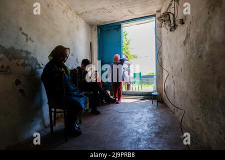 Eine alte Frau sitzt neben zwei Kindern am Eingang des Bunkers, wo sie in den Außenbezirken der Stadt abreisen. Lysychansík, Region Luhansk. 23. Mai 2022 Lysytschansk ist eine langgestreckte Stadt am rechten Ufer des Donezflusses in der Region Luhansk. Die Stadt ist Teil eines Ballungsraums, zu dem Severodonetsk und Rubizhne gehören; die drei Städte bilden zusammen einen der größten Chemiekomplexe der Ukraine. Die Stadt liegt etwa 7 km von der Front entfernt, und russische Truppen ziehen auf sie zu, die Stadt, wie Severodonetsk, ist fast isoliert. Die Russen versuchen, die Hauptstraße zu besetzen Stockfoto