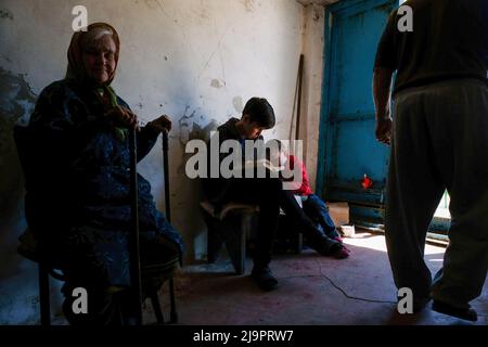 Eine alte Frau sitzt neben zwei Kindern am Eingang des Bunkers, wo sie in den Außenbezirken der Stadt abreisen. Lysychansík, Region Luhansk. 23. Mai 2022 Lysytschansk ist eine langgestreckte Stadt am rechten Ufer des Donezflusses in der Region Luhansk. Die Stadt ist Teil eines Ballungsraums, zu dem Severodonetsk und Rubizhne gehören; die drei Städte bilden zusammen einen der größten Chemiekomplexe der Ukraine. Die Stadt liegt etwa 7 km von der Front entfernt, und russische Truppen ziehen auf sie zu, die Stadt, wie Severodonetsk, ist fast isoliert. Die Russen versuchen, die Hauptstraße zu besetzen Stockfoto