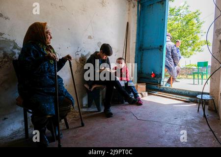 Eine alte Frau sitzt neben zwei Kindern am Eingang des Bunkers, wo sie in den Außenbezirken der Stadt abreisen. Lysychansík, Region Luhansk. 23. Mai 2022 Lysytschansk ist eine langgestreckte Stadt am rechten Ufer des Donezflusses in der Region Luhansk. Die Stadt ist Teil eines Ballungsraums, zu dem Severodonetsk und Rubizhne gehören; die drei Städte bilden zusammen einen der größten Chemiekomplexe der Ukraine. Die Stadt liegt etwa 7 km von der Front entfernt, und russische Truppen ziehen auf sie zu, die Stadt, wie Severodonetsk, ist fast isoliert. Die Russen versuchen, die Hauptstraße zu besetzen Stockfoto