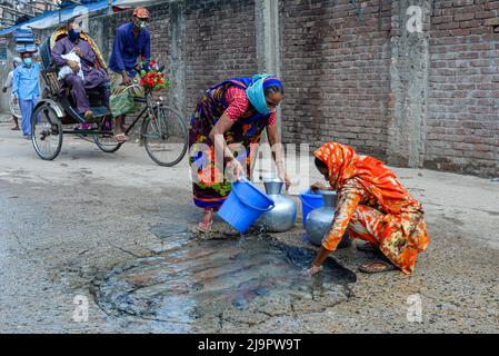 Frauen sammeln Trinkwasser von einem Wasserrohrbruch auf einer beschädigten Straße in Dhaka. Stockfoto