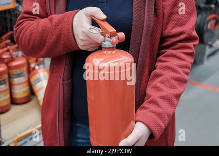 Die Frau in einem Geschäft entscheidet sich für einen kleinen Feuerlöscher. Nahaufnahme der Hände Stockfoto