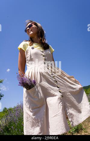Ein Mädchen mit einem Lavendelstrauß steht auf einem Feld und genießt die Sonne und den Sommer. Vertikales Foto. Stockfoto