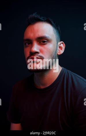 Latino Mann posiert mit blauen und roten Lichtern auf schwarzem Hintergrund. Porträt eines weißen Mannes mit Neonlicht. Vertikales Selbstporträt Stockfoto