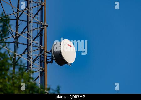 Runde Satellitenschüssel, montiert auf einer größeren Antennenstruktur gegen den blauen Himmel Stockfoto