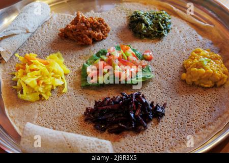 Injera serviert mit Gemüse und Linsen. Injera, das Grundnahrungsmittel Äthiopiens, ist ein Sauerteig-Fladenbrot aus Teffmehl. Stockfoto