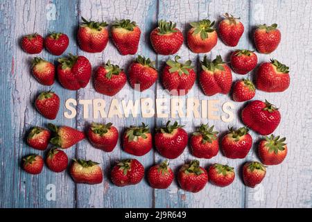 Viele rote Erdbeeren Früchte auf einem blauen Holzbrett und hölzerne Erdbeere Wort geschrieben Stockfoto