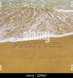 Konzeptbild - um Stress abzuwaschen, indem man einen Urlaub macht, während die Wellen an einem Sandstrand das Wort „Sorgen“ wegspülen. Stockfoto