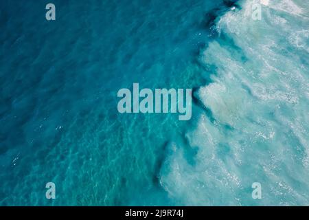 Draufsicht auf blaues transparentes Wasser im Ozean und Schaum durch Wellen, Luftaufnahme Stockfoto