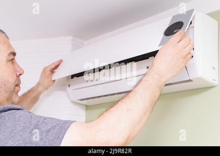 Ein Mann entfernt die Abdeckung der Klimaanlage für die Reinigung in Innenräumen Stockfoto