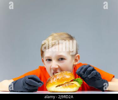 Der Junge lehnte sich über den Burger und will ihn beißen Stockfoto