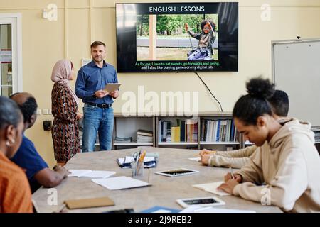 Horizontale Aufnahme einer multiethnischen Gruppe von Migranten, die während des Unterrichts an Englischkursen teilnehmen und Aufgaben erledigen Stockfoto