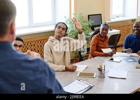 Junge Immigrant Black Student an Sprachkursen sitzen am Tisch Anhebung hanf Lehrer Frage zu stellen Stockfoto