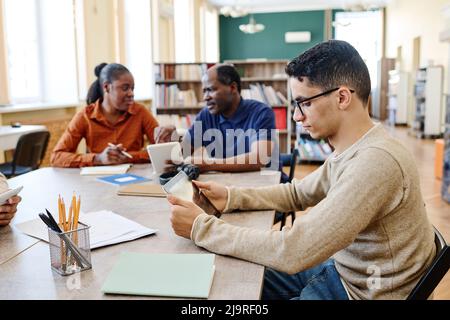 Junger Student aus dem Nahen Osten und seine schwarzen Mitschüler, die an einer Lektion für Einwanderer in der Bibliothek mit digitalen Tablets teilnehmen Stockfoto