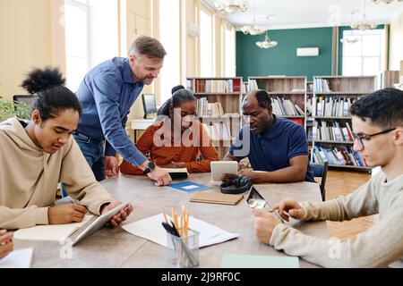 Reifer kaukasischer Englischlehrer, der Einwanderern hilft, Aufgaben während des Unterrichts zu verstehen Stockfoto