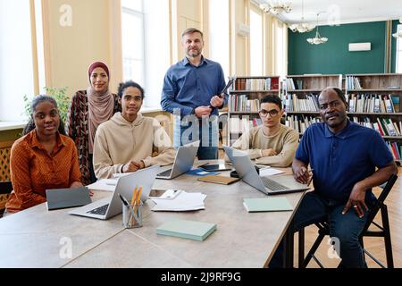 Gruppenporträt eines modernen Englischlehrers und multiethnischer Einwanderer, die in der Bibliothek Unterricht haben und die Kamera betrachten Stockfoto