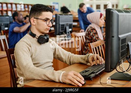 Eine Gruppe ethnisch diverser Studenten, die in der modernen Universitätsbibliothek sitzen und an Computern arbeiten Stockfoto