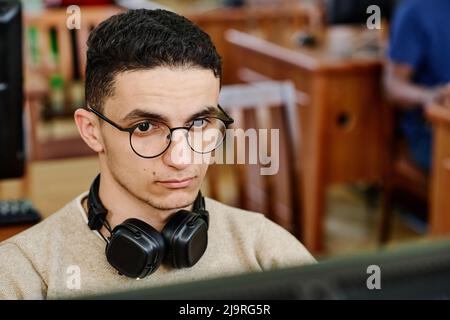 Nahaufnahme eines ernsthaften Studenten aus dem Nahen Osten, der Kopfhörer trägt und am Computer in der Bibliothek arbeitet Stockfoto