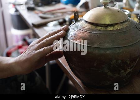 Restaurierung eines alten Kännchen aus Metall und anderen Antiquitäten, berührt die Hand eines Mannes den Krug, in einer Werkstatt Stockfoto