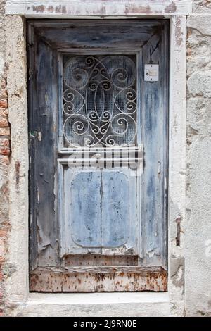 Italien, Venedig. Alte blaue Holztür mit Metalldesign im Fenster. Stockfoto