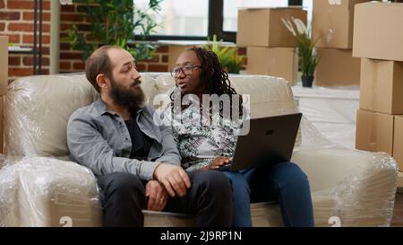 Diverse Paare suchen Dekor Inspiration und Möbel auf der Website, Online-Shopping auf Laptop. Umzug in der Wohnung gekauft auf Hypothek zusammen und Dekoration Wohnung. Handgeführte Aufnahme. Stockfoto