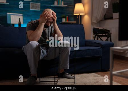 Frustrierter Mann, der im Fernsehen Sport sieht und traurig ist über den Verlust des Meisterschaftsspiels der Fußballmannschaft. Fußballfans fühlen sich über die Niederlage des Spiels verärgert und emotional. Stockfoto