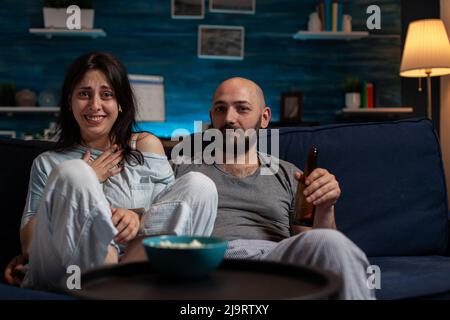 POV von Freundin und Freund, der Film auf dem Fernsehkanal ansieht, um Spaß mit Freizeitaktivitäten zu haben. Fröhliches Paar, das gerne Filme im Fernsehen ausgestrahlt, Bier und Popcorn getrunken hat. Stockfoto